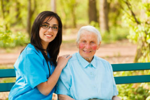 Kind elderly lady with caring nurse sitting both on bench in a park.